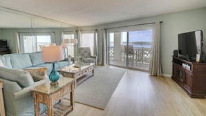 A spacious living room with a sofa, armchair, and coffee table, a television, and a large window with a view of the water. - 554 El Matador 1 Bedroom Condo by RedAwning (Fort Walton Beach)