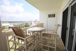 A balcony with wicker furniture, a white door, and a view of a body of water and buildings. - 554 El Matador 1 Bedroom Condo by RedAwning (Fort Walton Beach)