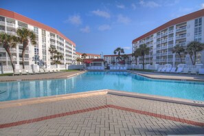 A hotel with a central swimming pool surrounded by lounge chairs and palm trees. - 440 El Matador 2 Bedroom Condo by RedAwning (Fort Walton Beach)