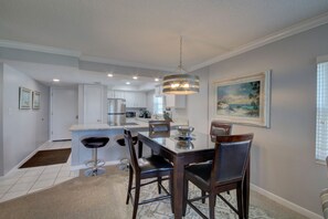 A modern kitchen with white cabinets, a stainless steel refrigerator, and a dining area with a table and chairs. - 440 El Matador 2 Bedroom Condo by RedAwning (Fort Walton Beach)