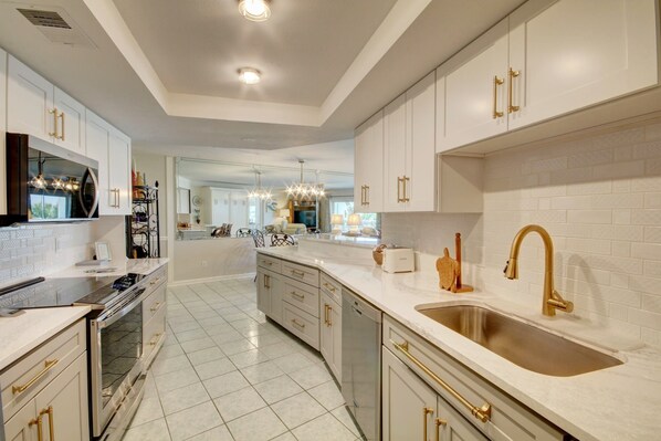 A spacious kitchen with white cabinets, a stainless steel sink, and a modern chandelier.