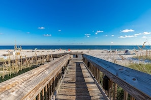 Een houten looppad dat naar een zandstrand leidt, met parasols en ligstoelen.