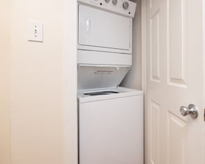 Een compacte, witte wasmachine en droger gestapeld in een kleine wasruimte, met een deur aan de rechterkant.