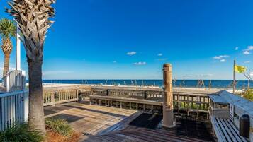A wooden pier with a view of the ocean, a palm tree, and a flag.