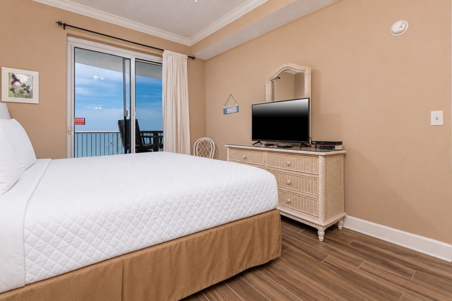 Habitación de hotel con cama, televisor en una cómoda, balcón con una silla y un espejo montado en la pared.