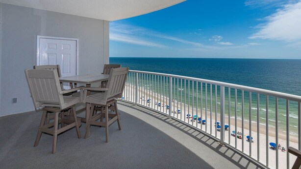 A balcony with a table and chairs, overlooking a beach with umbrellas and people.