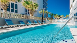 A swimming pool with lounge chairs, palm trees, and a building in the background.