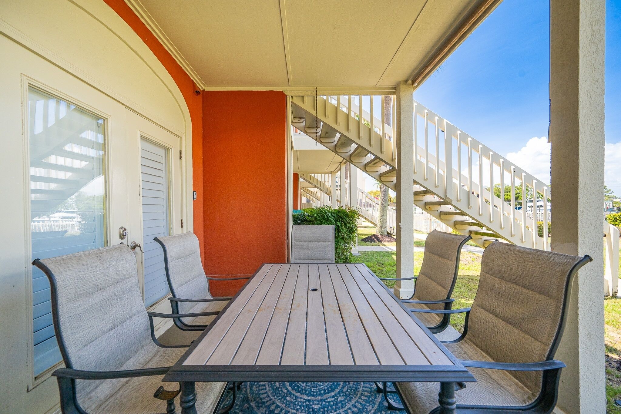 Une terrasse extérieure couverte, avec une table et des chaises, un escalier et une vue sur un bâtiment en arrière-plan.