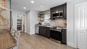 Une cuisine moderne avec des meubles de couleur sombre, des appareils électroménagers en acier inoxydable et une table à manger en bois.