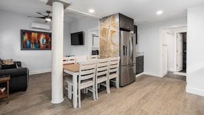 Une cuisine moderne avec un revêtement mural en marbre, des appareils en acier inoxydable et un coin repas doté de chaises blanches.