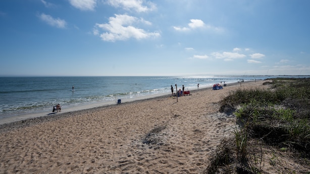 Une plage de sable où se trouvent des gens, un ciel dégagé et l’océan.