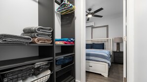 Un placard bien rangé, doté d’étagères et d’une tringle pour suspendre les vêtements, un lit recouvert d’une couverture à rayures et un ventilateur de plafond dans une chambre.