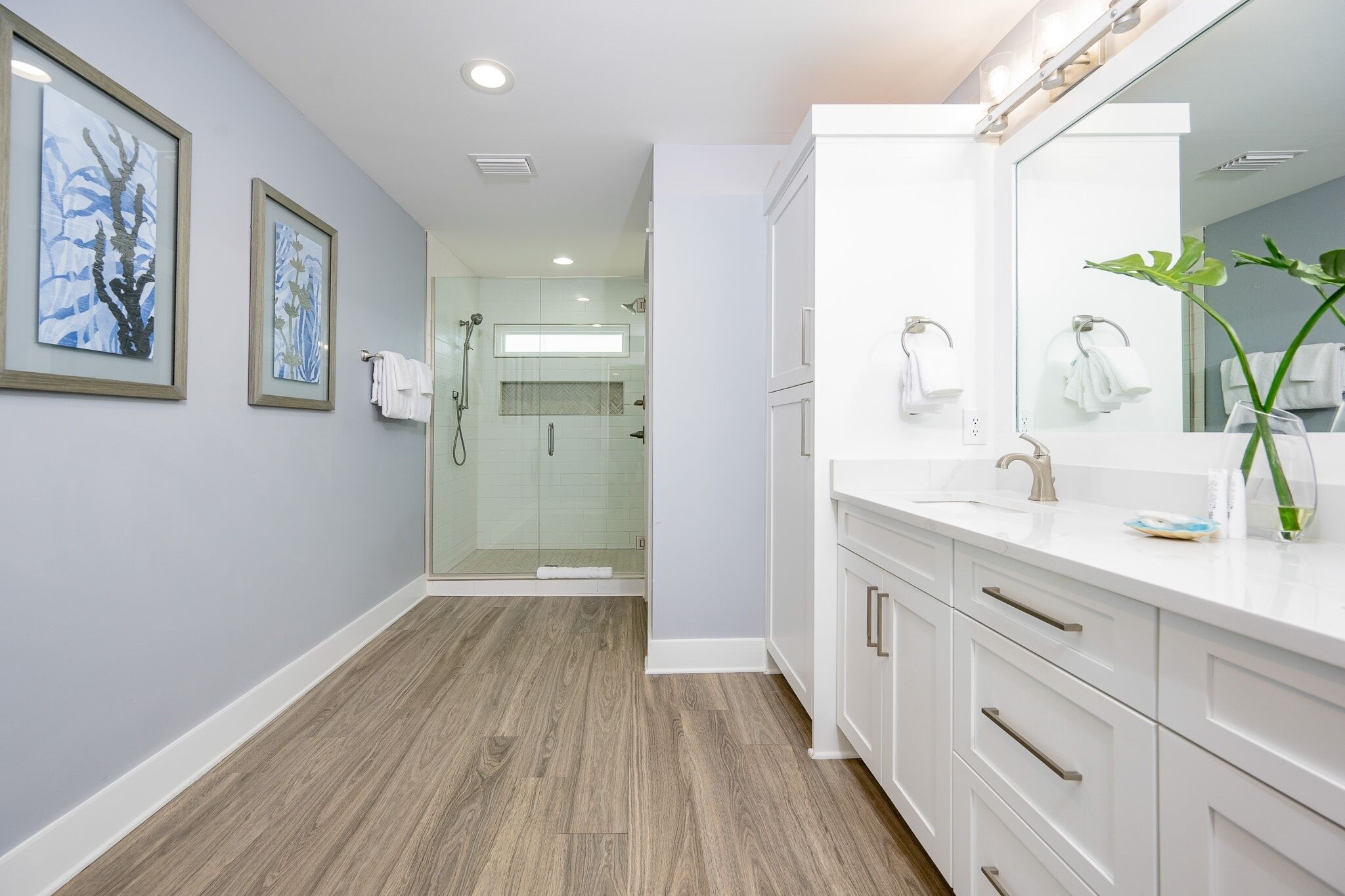 Un baño moderno con ducha de vidrio, muebles blancos y cuadros en la pared.