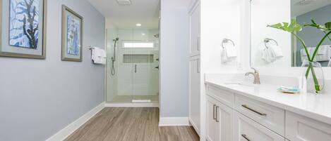 Un baño moderno con ducha de vidrio, muebles blancos y cuadros en la pared.