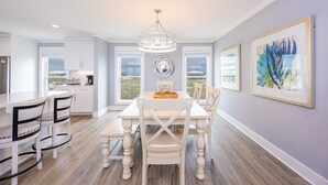A modern kitchen with white cabinetry, a dining table with chairs, and a chandelier. - Blue Hideaway 2888 3 Bedroom Home (Gulf Shores)