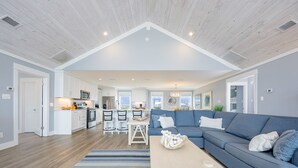 A spacious living area with a large blue sofa, a coffee table, and a kitchen in the background. - Blue Hideaway 2888 3 Bedroom Home (Gulf Shores)