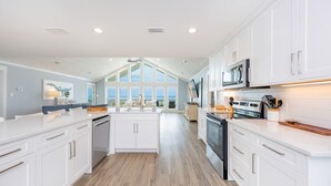 A spacious kitchen with white cabinetry, a central island, and a large window providing a view. - Blue Hideaway 2888 3 Bedroom Home (Gulf Shores)