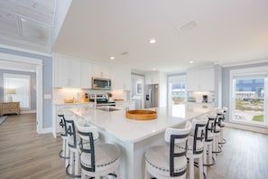 Une cuisine moderne avec des meubles blancs, un îlot central doté de tabourets et une grande fenêtre offrant une vue dégagée.