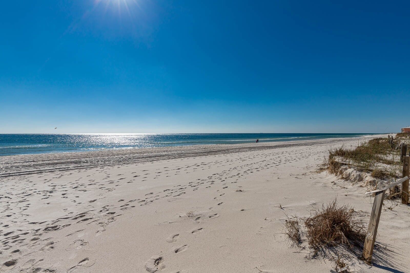 A beach with footprints, a wooden fence, and a clear sky.