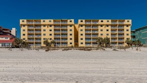 Un hotel de varios pisos con balcones, situado en una playa arenosa con palmeras.