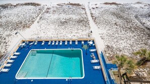 Vista aérea de un área de piscina con agua azul, rodeada de sillas de descanso y una terraza.