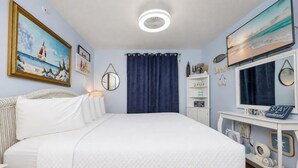 Un dormitorio con cama, televisión, escritorio con ordenador y diversos adornos.