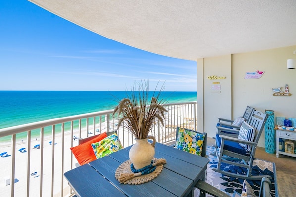 A balcony with a view of the ocean, a table with a vase, and a chair.