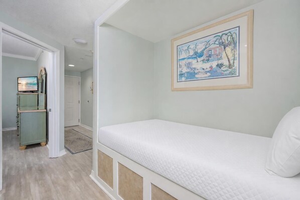 A bedroom with a bed, a painting, and a television in a hallway.
