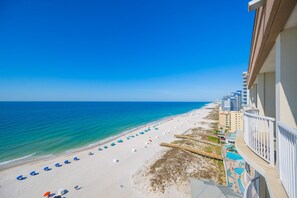 A beach view from a balcony with a clear sky, a sandy beach, and a pool area.