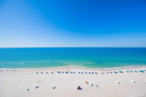 A beach with rows of umbrellas and sun loungers, a clear blue sky, and calm ocean waters. - Royal Palms 1404 1 Bedroom Condo (Gulf Shores)