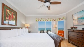 Habitación de hotel con una cama grande, un ventilador de techo, vista al océano, un aparador de madera y un cuadro en la pared.