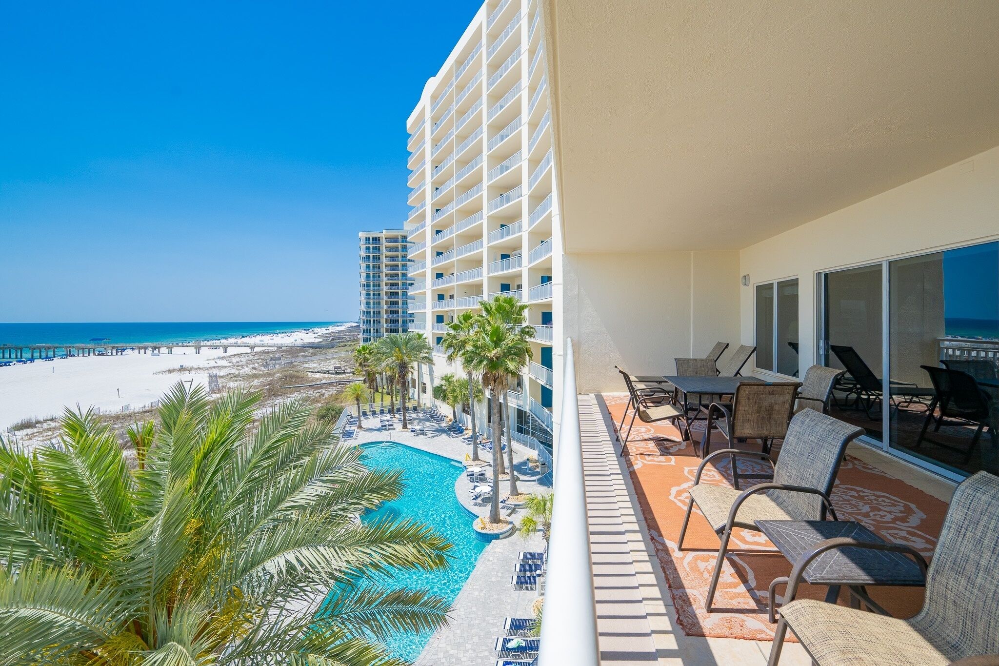 Un balcon d’hôtel avec vue sur la plage et l’océan, des sièges d’extérieur et une piscine.