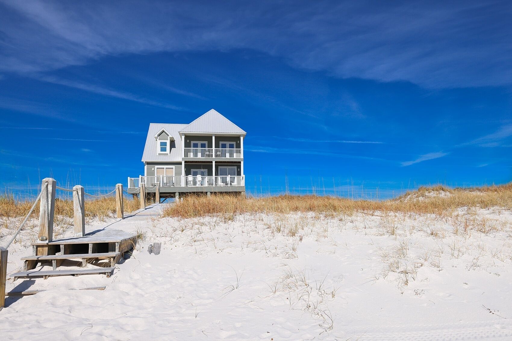 Ein Strandhaus mit einer Holzterrasse und einer Treppe, die zu einem Balkon führt.