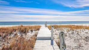 A wooden boardwalk leading to a beach with sand dunes and a clear blue sky. - Windswept 4 Bedroom Home (Orange Beach)