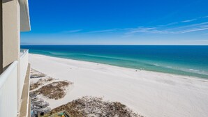 Blick auf den Strand vom Balkon aus, mit blauem Himmel und ruhiger See.
