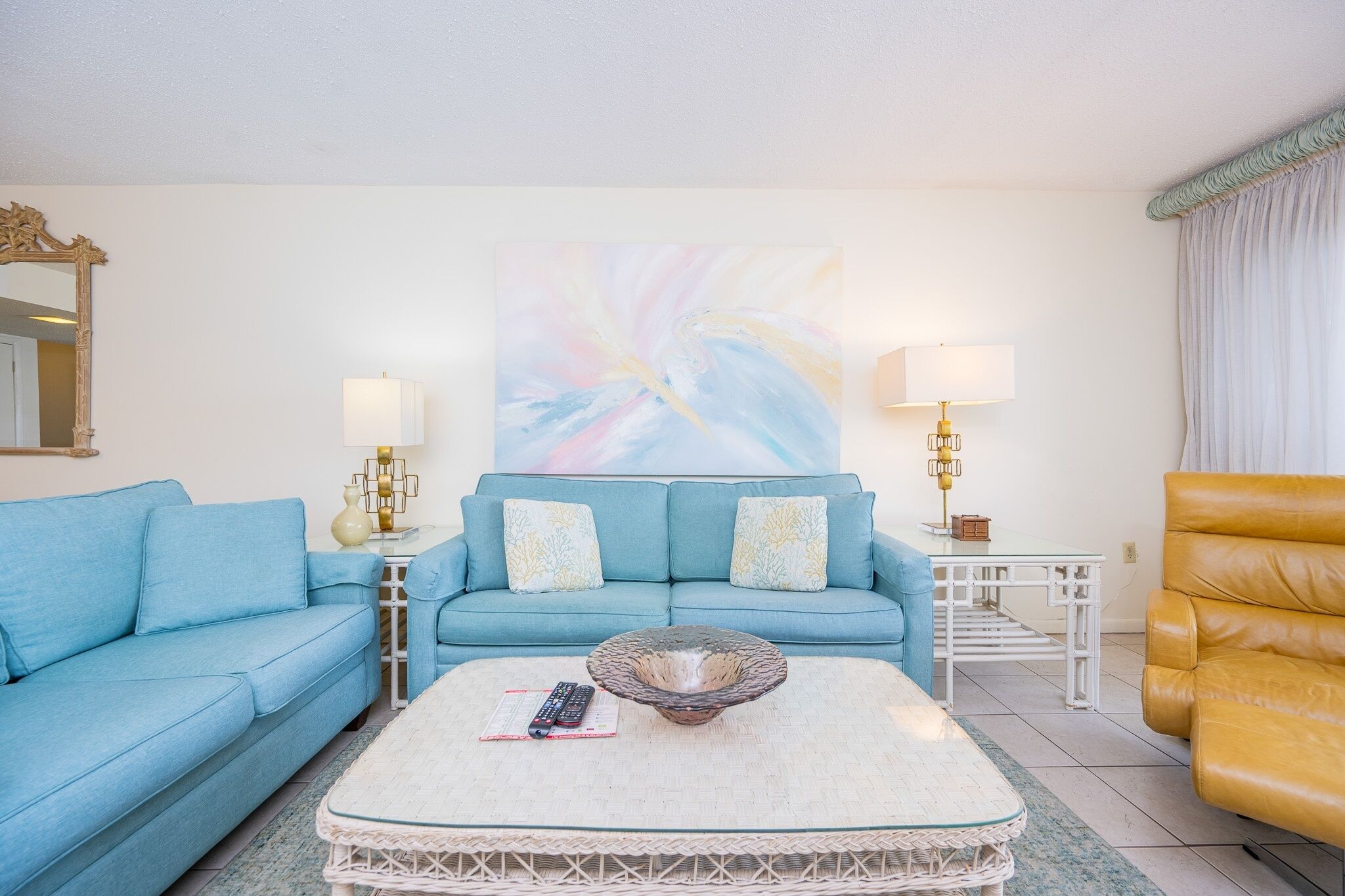 Una sala de estar con un sofá azul, una mesa de centro, un sillón amarillo y un cuadro en la pared.