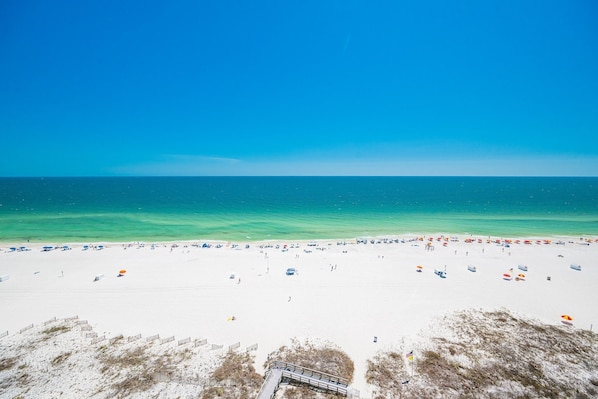 A beach with a clear sky, sandy shore, and a wooden walkway leading to the water.