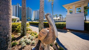 Eine große Vogel-Skulptur in einer angelegten Grünfläche mit Palmen und einem Gebäude im Hintergrund.