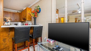 Ett modernt kök med träskåp, en matplats med två svarta stolar, ett glasbord och en tv med platt skärm.