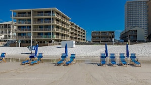 Ett hotell vid stranden med flera balkonger, en sandstrand med blå solstolar och en klarblå himmel.
