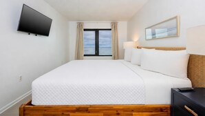 A hotel room with a bed, a TV, a window with curtains, a lamp, and a picture on the wall. - Island Sunrise 365 2 Bedroom Condo (Gulf Shores)