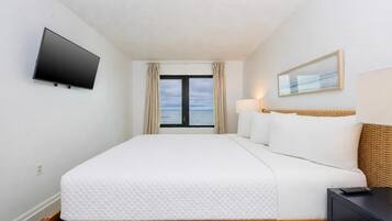 Une chambre d’hôtel avec un lit, une télévision, une fenêtre avec des rideaux, une lampe et un tableau au mur.