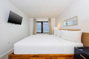 Une chambre d’hôtel avec un lit, une télévision, une fenêtre avec des rideaux, une lampe et un tableau au mur.