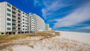 A beachfront hotel with multiple balconies, a sandy beach, and a clear blue sky. - Island Sunrise 365 2 Bedroom Condo (Gulf Shores)
