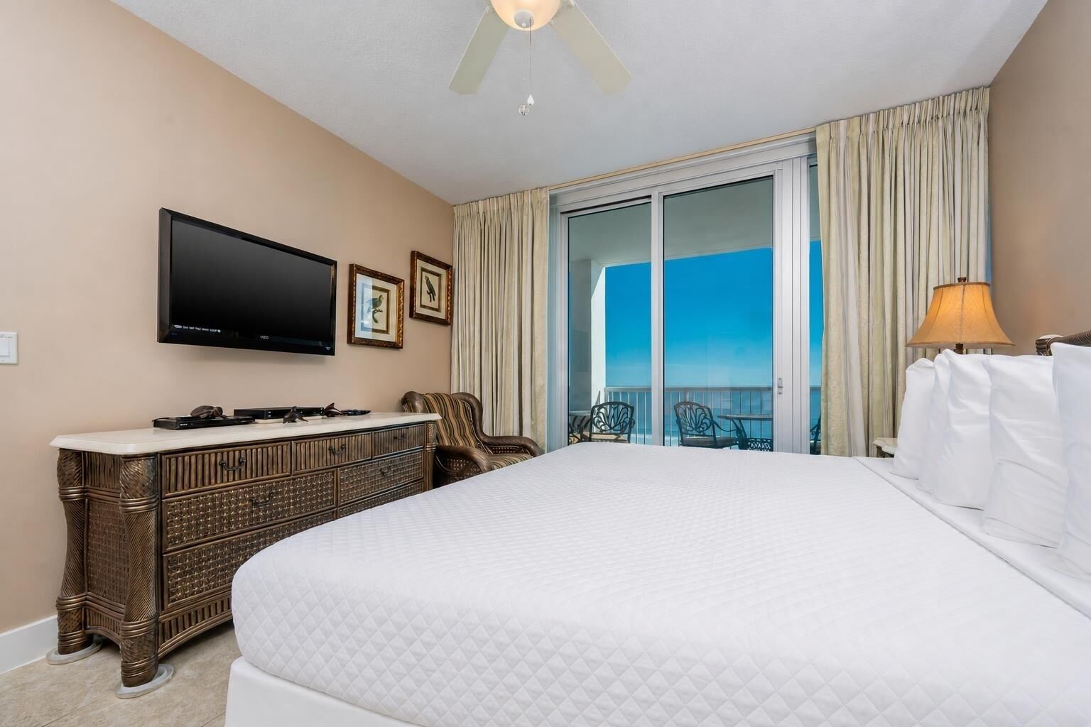 Habitación de hotel con cama, televisor de pantalla plana, cómoda, silla y balcón con vistas.