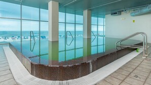 An indoor infinity pool with clear glass walls, a marble edge, and a metal handrail. - Island Tower 601 3 Bedroom Condo (Gulf Shores)