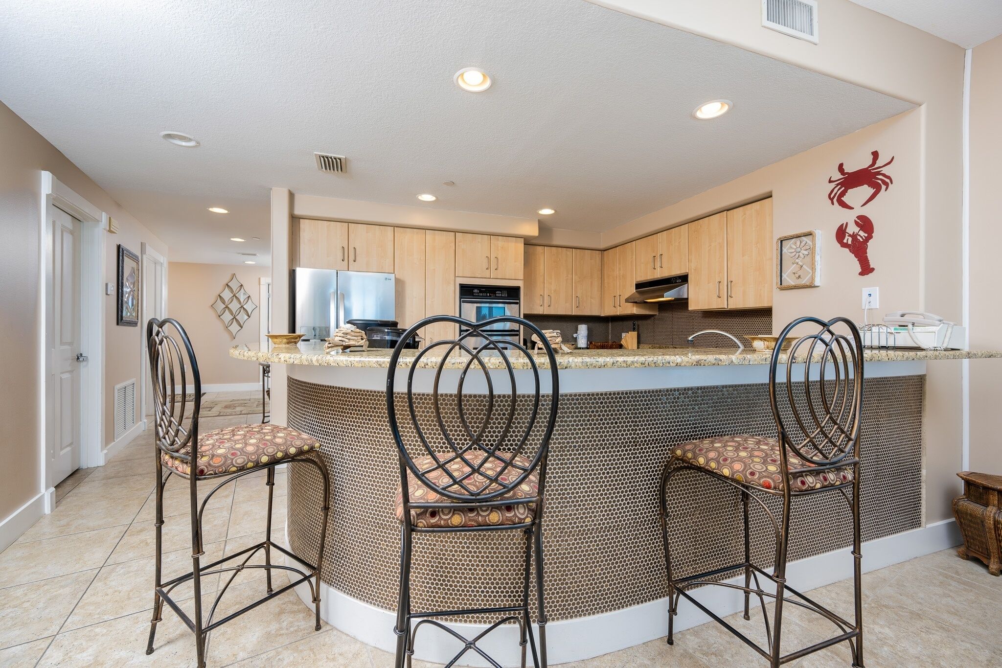 A kitchen with a central island, three bar stools, wooden cabinets, and a wall-mounted crab decoration.
