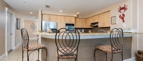 A kitchen with a central island, three bar stools, wooden cabinets, and a wall-mounted crab decoration.