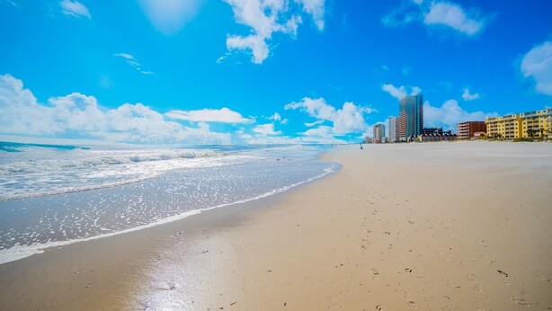 A beach with a clear sky, waves, and buildings in the background. - Island Tower 601 3 Bedroom Condo (Gulf Shores)