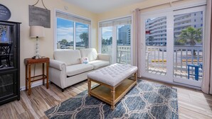 Una sala de estar con un sofá blanco, un banco de madera, una lámpara y un ventanal con vistas a la ciudad.
